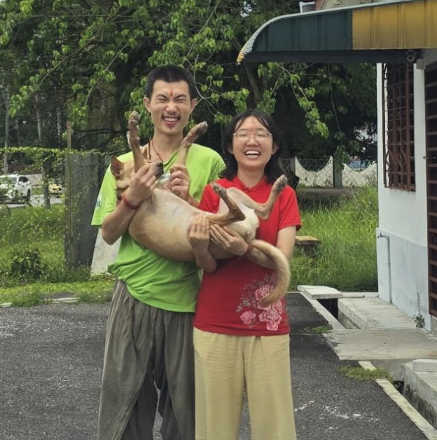 Wan Hui and Andrew laughing outdoors while holding Nandi.